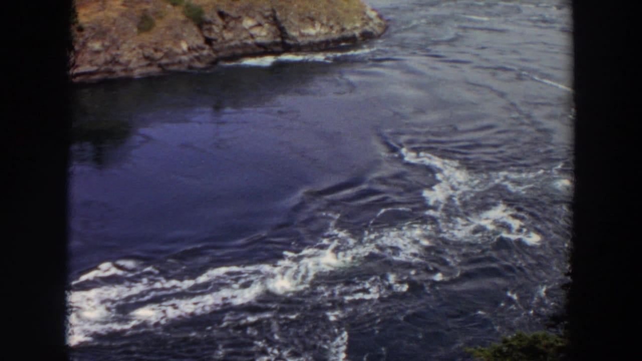 1964 Washington home-movie frame with swirling water patterns and a rocky outlet edge visible at the top.