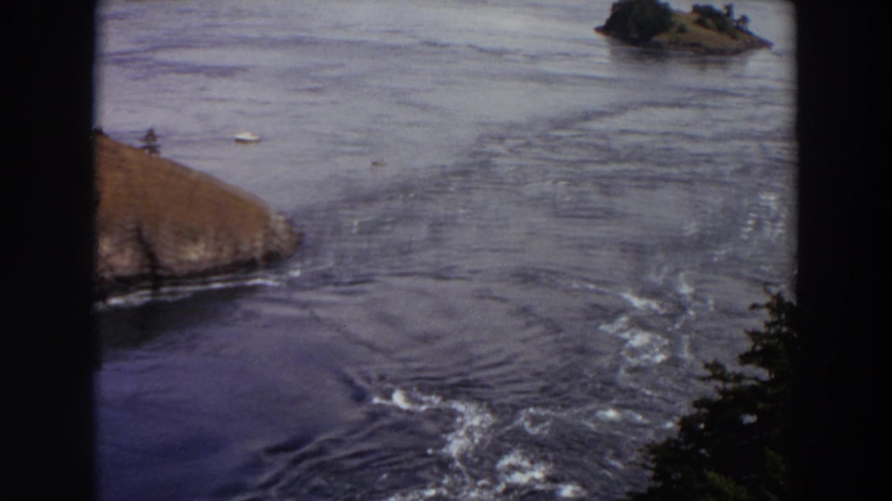 Wide river current with rocky shore, small islands, and dark film-frame borders.
