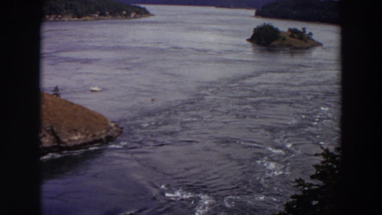 Washington river scene on 8mm film, with visible current patterns around a rocky point and small wooded islands.