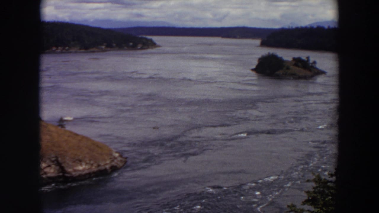 Soft 8mm frame of a Washington waterway with forested hills, a small island, and rippling current.