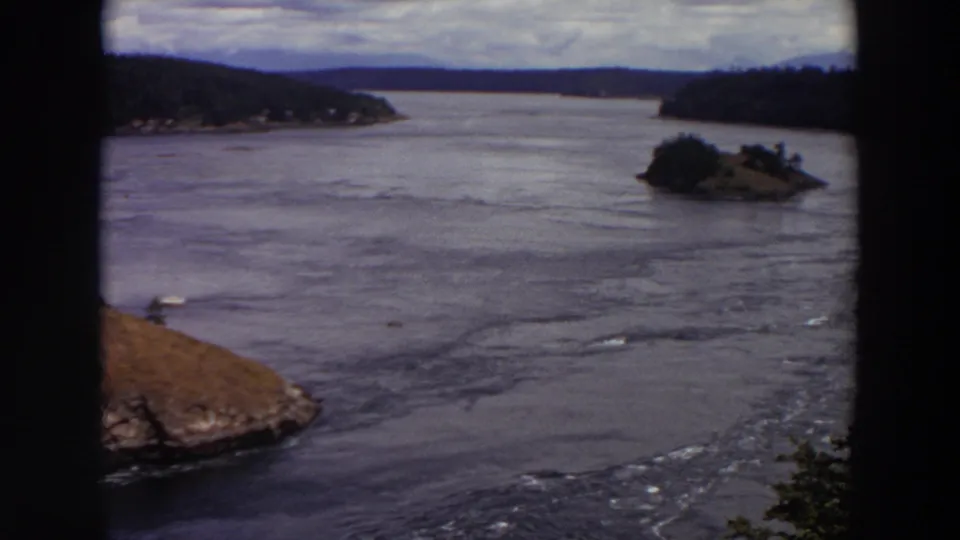 Soft 8mm frame of a Washington waterway with forested hills, a small island, and rippling current.