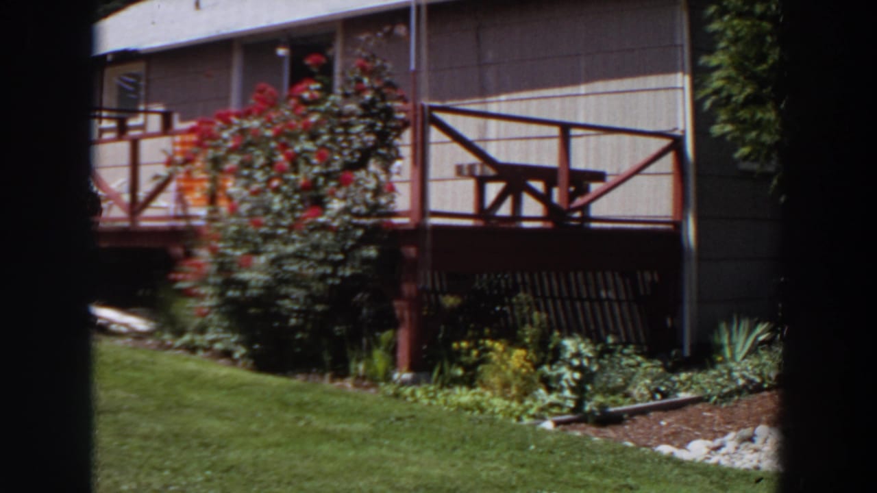 Red-railed porch with picnic table above a sunny lawn and flower garden.