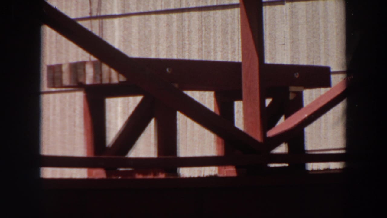 1964 Washington 8mm frame showing a close red-painted wooden bench or stool detail against a light vertically grooved wall.