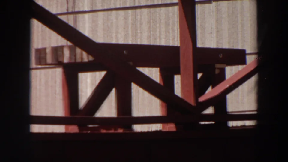 1964 Washington 8mm frame showing a close red-painted wooden bench or stool detail against a light vertically grooved wall.