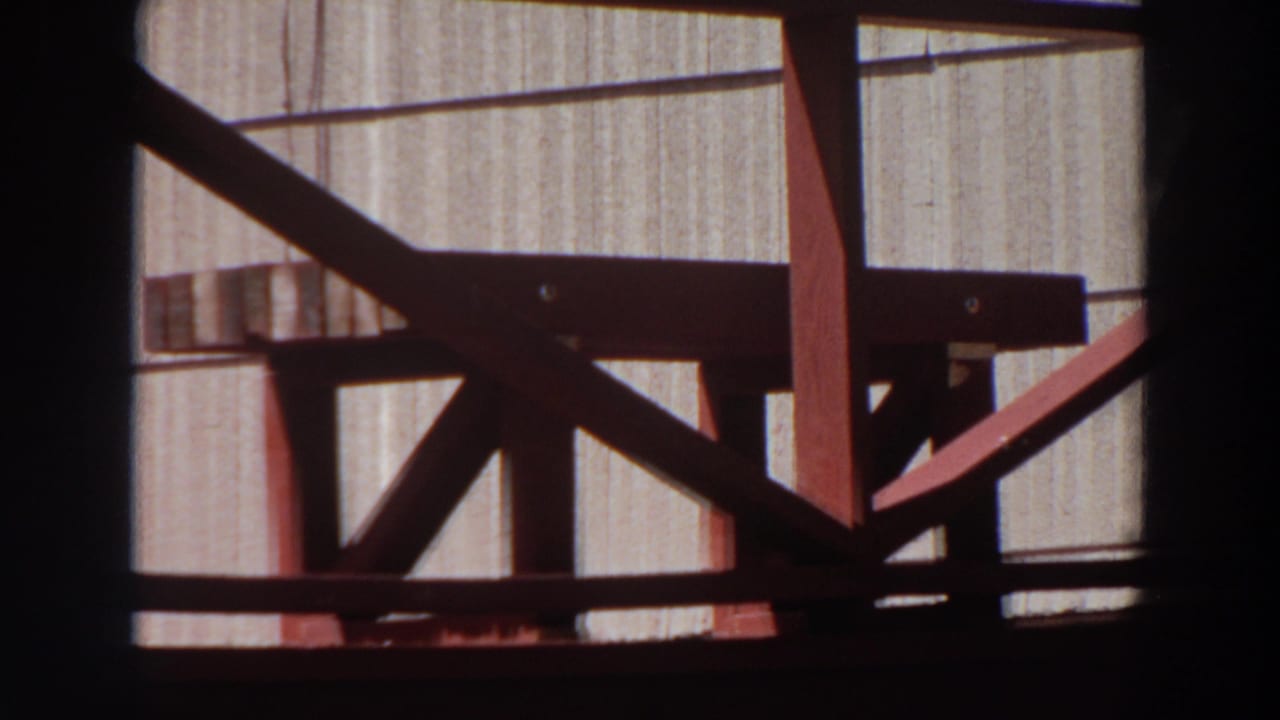 Close 1964 Washington 8mm view of red-painted wooden supports and rails with a light grooved wall in the background.