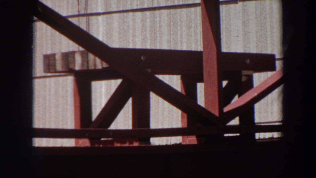 1964 Washington 8mm frame showing red-painted wooden bench or stool construction against a pale grooved wall.