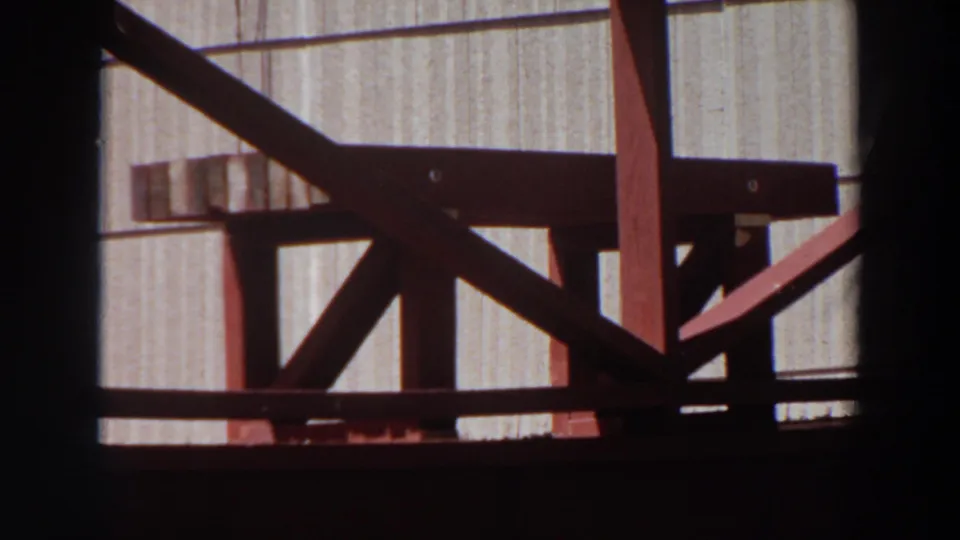 1964 Washington 8mm frame showing red-painted wooden bench or stool construction against a pale grooved wall.