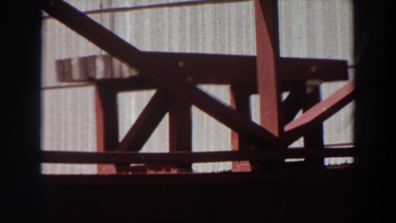 Red wooden porch or railing beside a light exterior wall, partly framed by dark film edges.