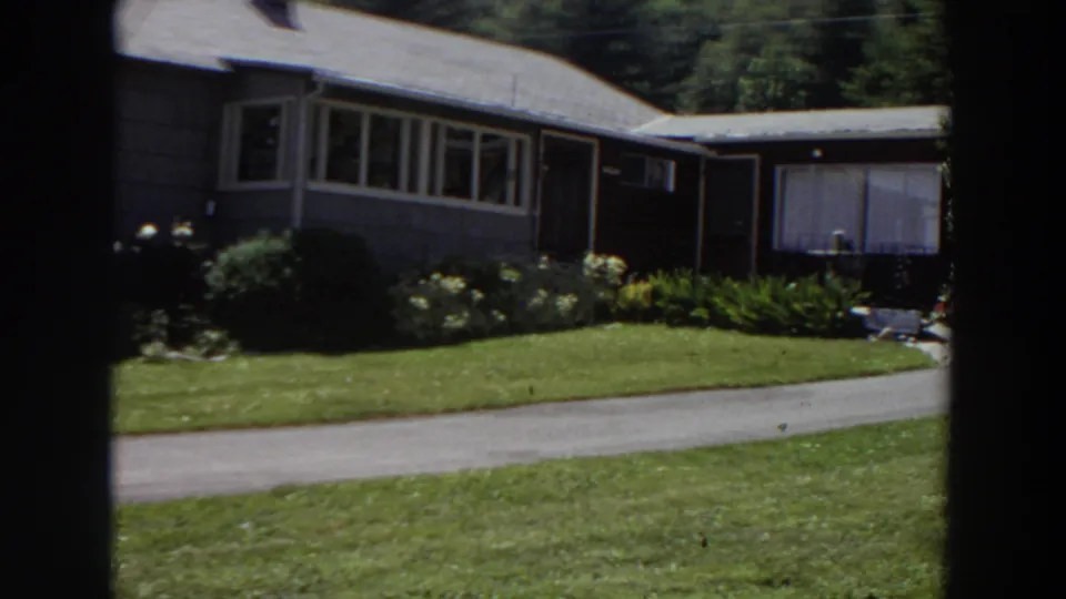 1964 Washington 8mm frame showing the pan reaching the house side, with long windows, flower beds, lawn, and driveway visible.