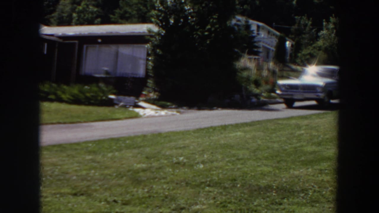 A light-colored station wagon appears at the right edge of a 1964 Washington residential driveway scene with house, trees, and lawn.