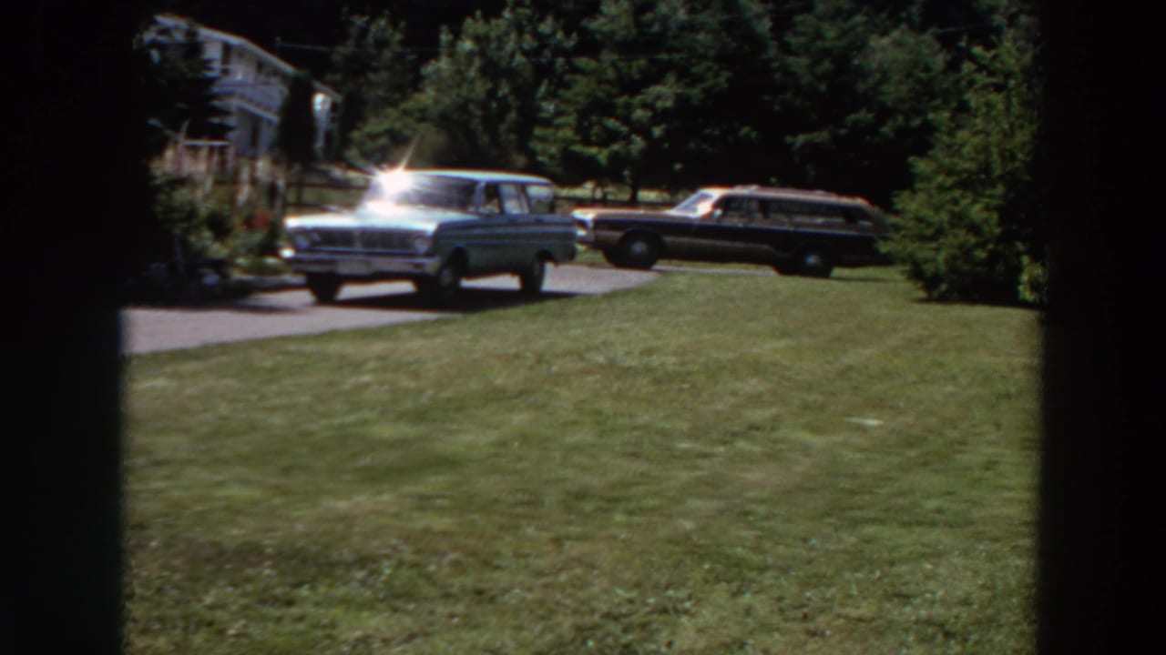 Two station wagons parked by a driveway beyond a green lawn.