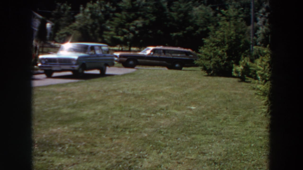 1964 Washington suburban yard view with two station wagons on a driveway, trees behind them, and a shaded vertical obstruction in frame.