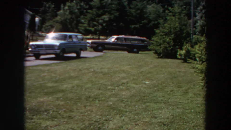 1964 Washington suburban yard view with two station wagons on a driveway, trees behind them, and a shaded vertical obstruction in frame.