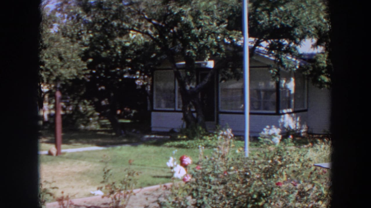 White house with enclosed porch partly framed by trees and garden shrubs.