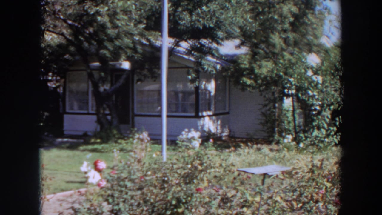 1964 Washington frame with a white-sided house, enclosed porch, foreground roses, red hydrant, vertical pole, and small garden table.