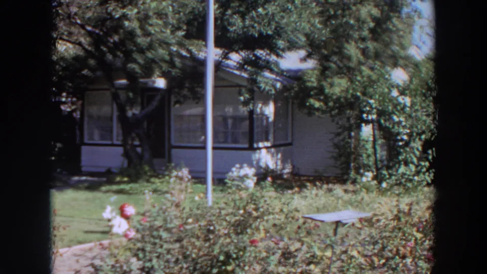 1964 Washington frame with a white-sided house, enclosed porch, foreground roses, red hydrant, vertical pole, and small garden table.