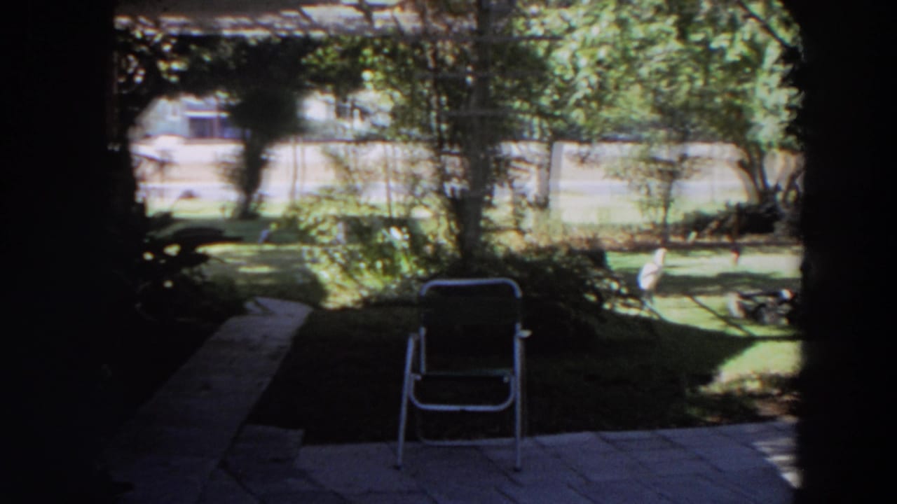 Shaded porch view of a sunlit backyard with a folding chair on a stone patio.