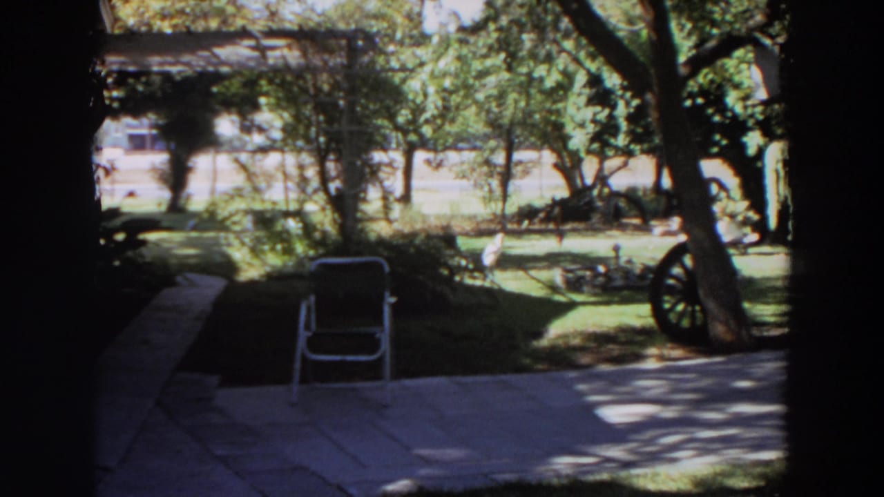 1964 Washington backyard frame with a folding chair on the patio and garden decor under trees.