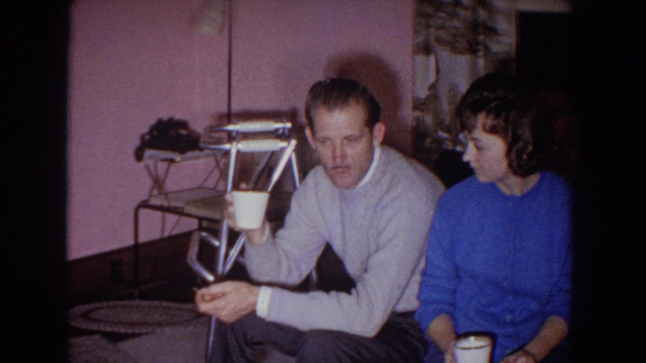 Man and woman seated in a pink-walled living room holding cups.