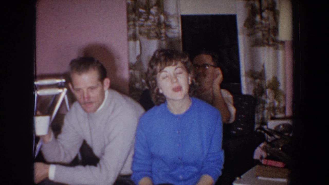 Two adults seated in the foreground with another man visible behind them.