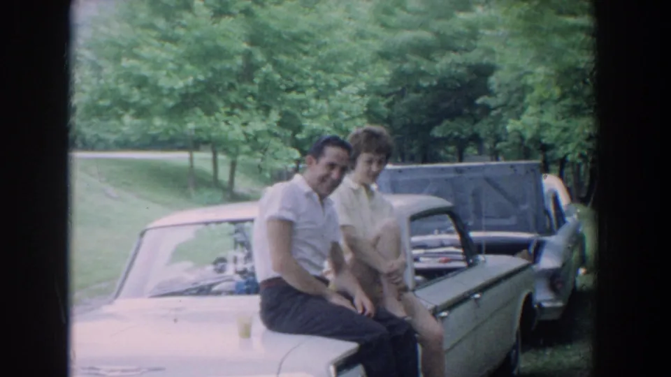 In Fallston, Maryland home-movie footage from 1965, a young couple sits on a light-colored car as another car stands behind them.