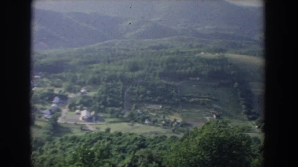 1965 Fallston, Maryland home-movie frame showing a small rural settlement below wooded hills, with fields and roads seen from above.