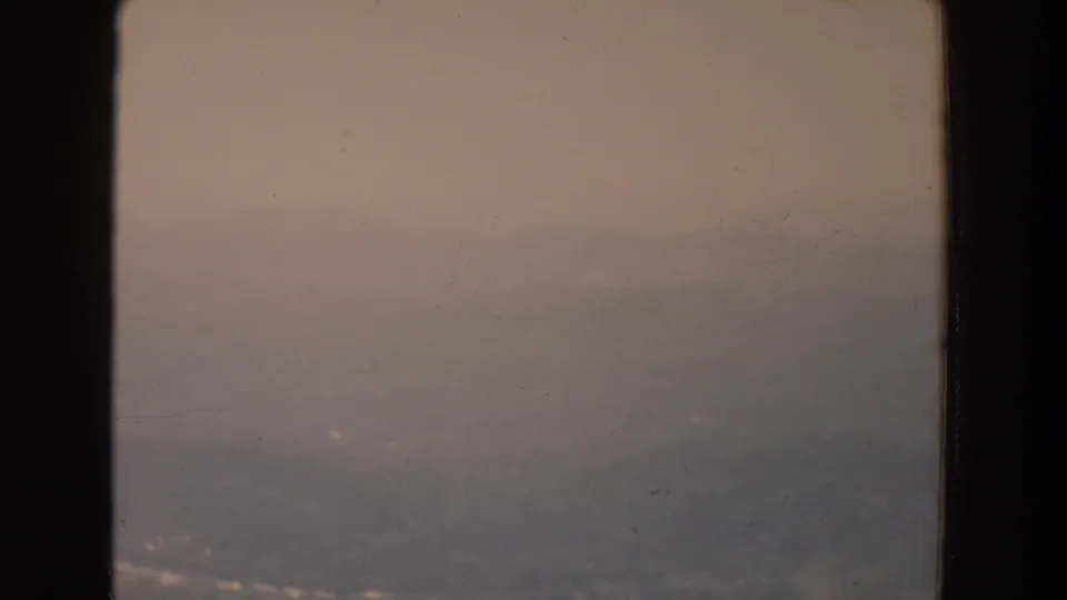 1965 Fallston, Maryland metadata view of a hazy grey ridge through a dark window frame on faded 8mm film.