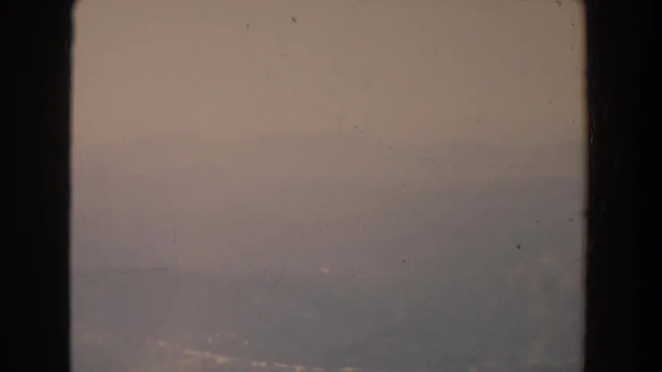 A pale, fog-softened horizon and distant ridge are seen through a window frame in 1965 Fallston, Maryland home-movie footage.