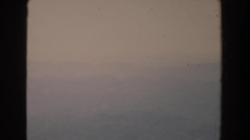 The lower frame shows a fog-muted landscape with a faint ridge line, viewed through a dark interior window frame on 8mm film.
