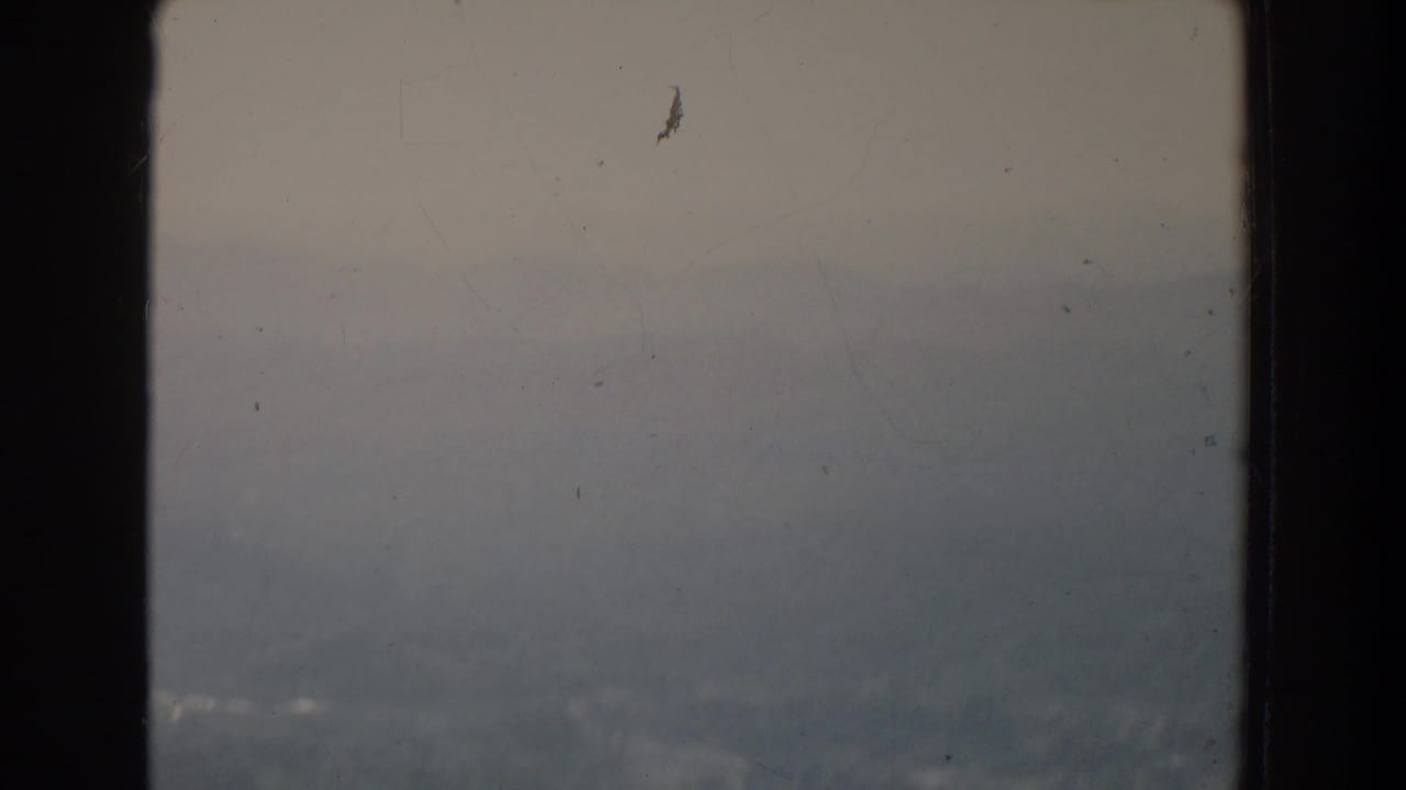 Hazy hills and valley seen through a dark aircraft window frame.