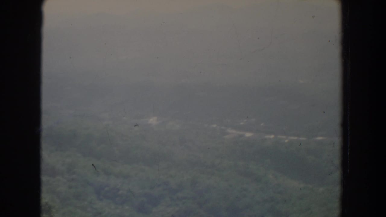Hazy forested hills and distant mountains seen through a soft, scratched film frame.