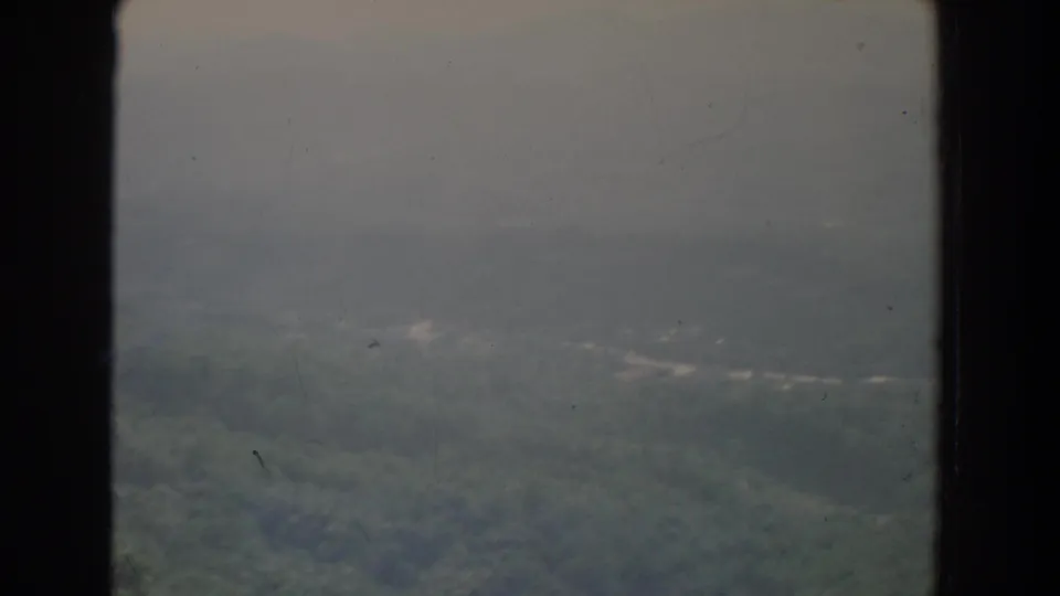 1965 Fallston, Maryland home-movie frame showing hazy wooded hills and distant mountain ridges under an overcast sky.