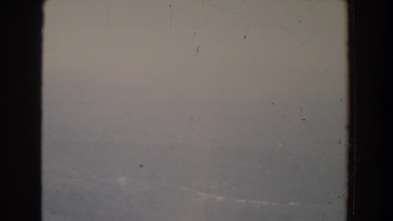 Overexposed hazy sky and faint distant landscape behind dark film-frame borders.