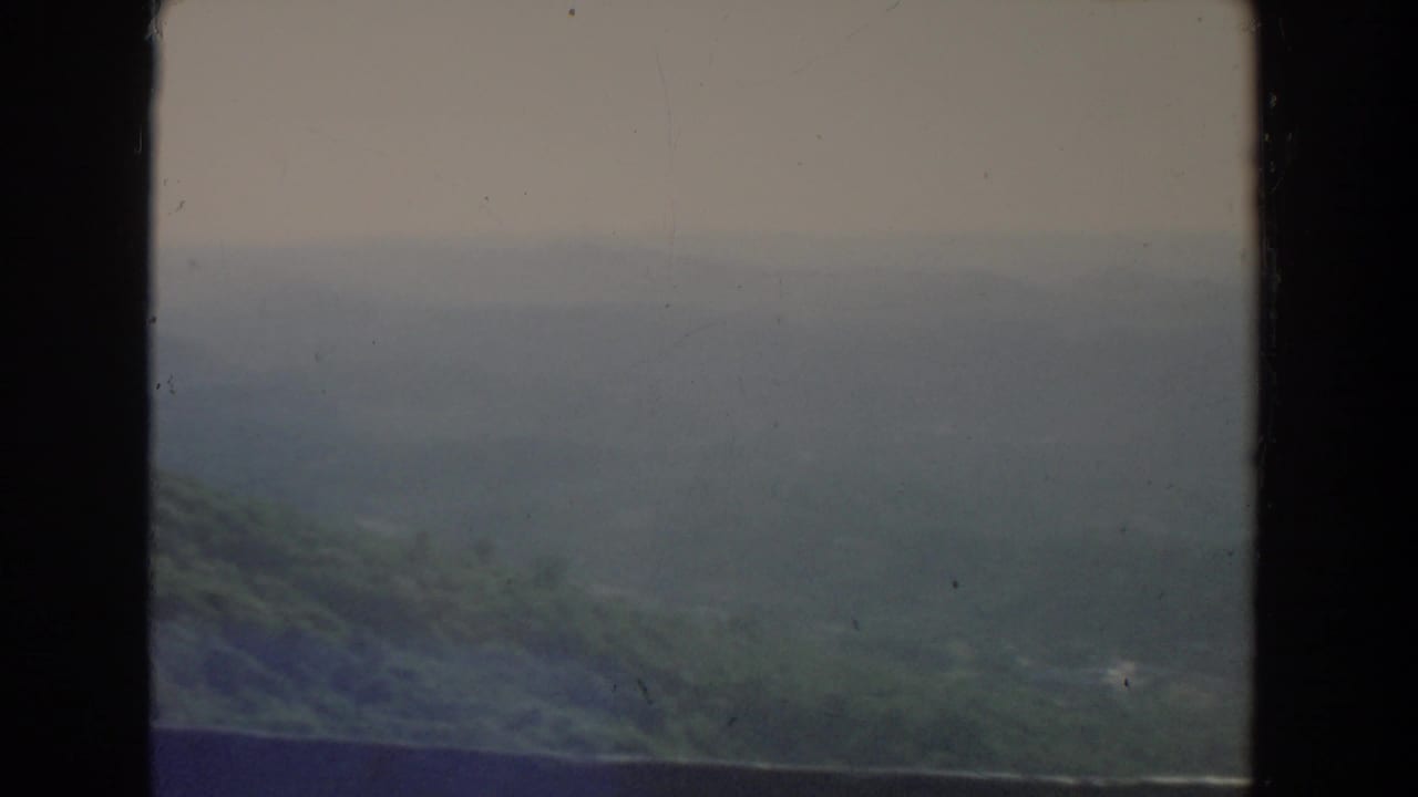 Hazy green hills under a cloudy sky within dark film-frame borders.