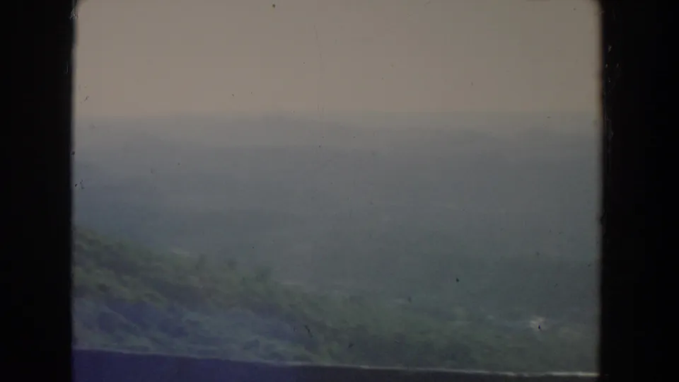 1965 8mm home-movie frame of hazy hills and overcast sky in the Fallston, Maryland metadata area, with dark projected borders.