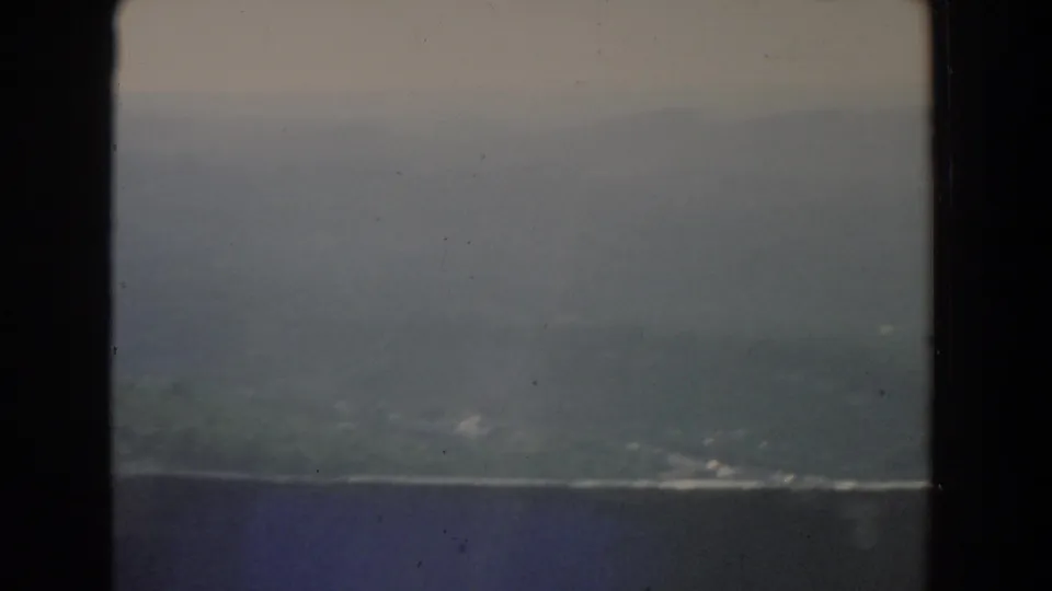 Soft 8mm view of distant hills and muted sky, with a dark band across the lower frame and visible projector-edge borders.