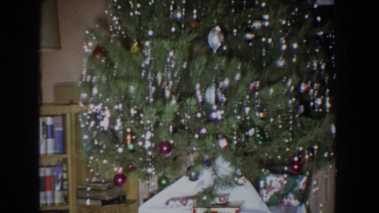 Trimmed Christmas tree with ornaments and tinsel above wrapped gifts in a home interior.