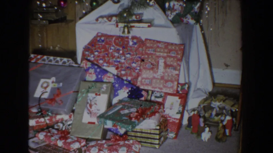 1965 Fallston, Maryland frame focused on wrapped holiday gifts under a decorated tree, with a small nativity scene at lower right.