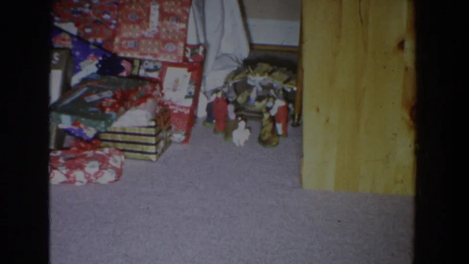 1965 Fallston, Maryland frame with stacked wrapped gifts, bows, carpet, wood paneling, and small holiday figurines.