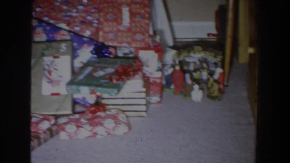 1965 Fallston, Maryland home-movie view of brightly wrapped Christmas presents with bows and small figurines on a carpet.