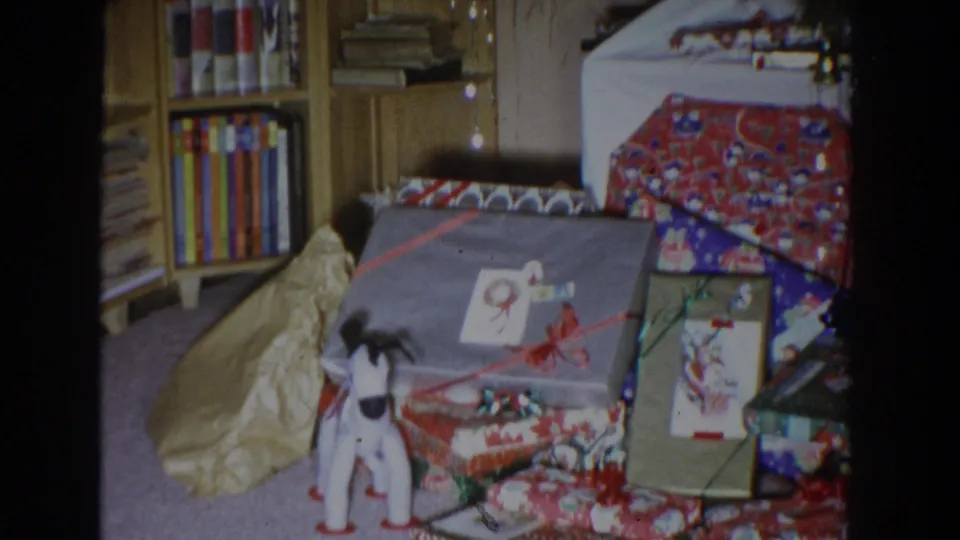 Wrapped gifts, ribbon, a toy dog, and shelving fill the frame in this Fallston, Maryland Christmas home-movie still.