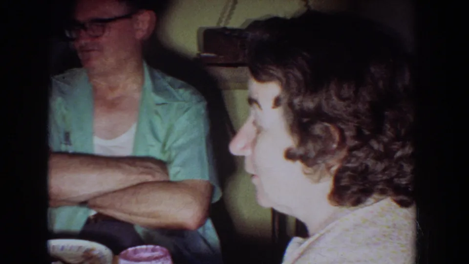 1965 Fallston, Maryland home-movie frame showing adults seated in a kitchen during a casual family conversation.