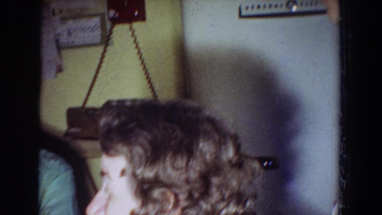 Curly-haired woman in profile near a kitchen wall with a red wall phone above her.