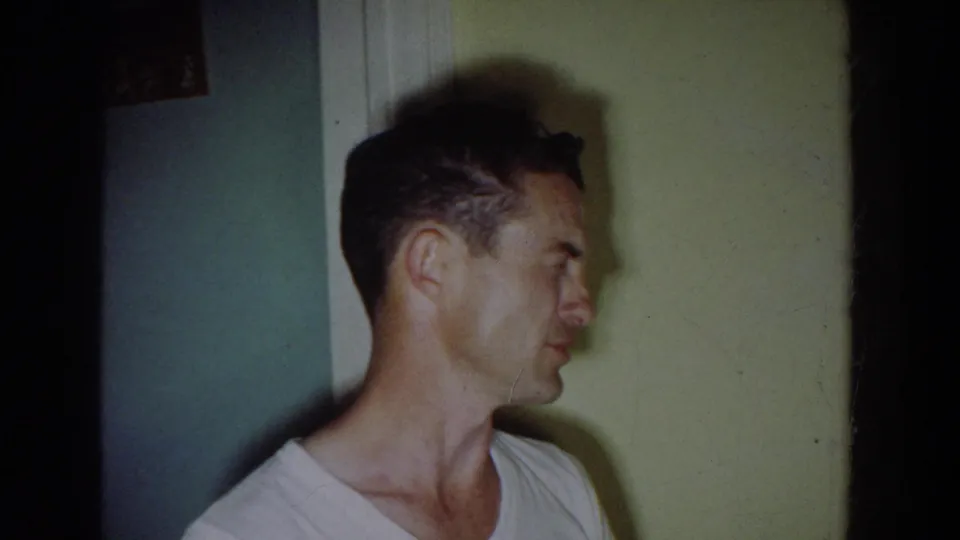 Fallston home-movie frame showing a man in profile seated by a kitchen doorway during the family gathering.