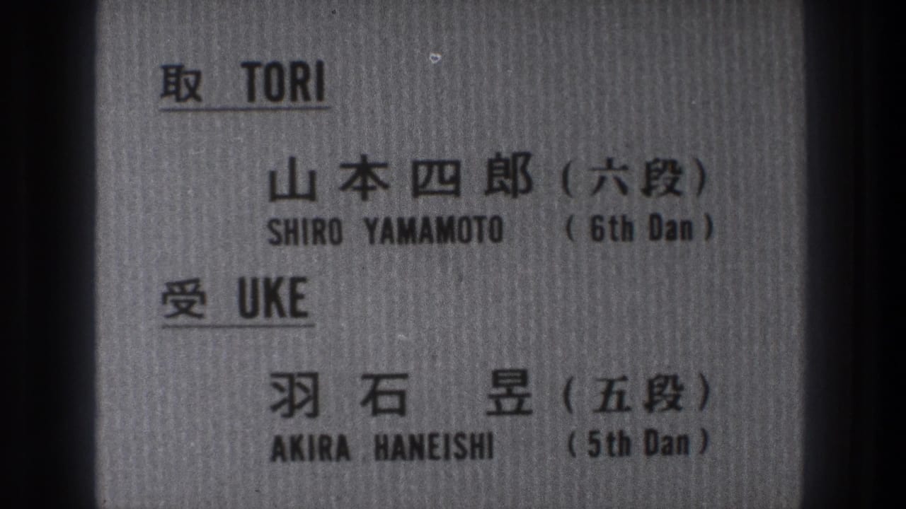1971 8mm frame of a gray printed card identifying Shiro Yamamoto and Akira Haneishi in Japanese and English.