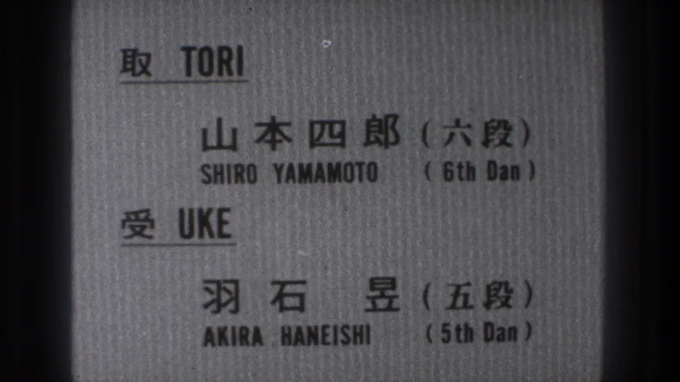 1971 8mm frame of a gray printed card identifying Shiro Yamamoto and Akira Haneishi in Japanese and English.
