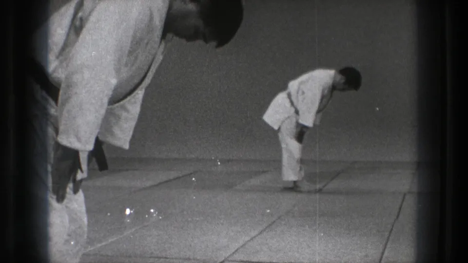 1971 Tokyo home-movie frame showing the instructor bending into a formal bow in a plain matted training space.
