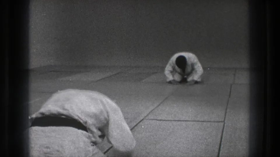1971 Tokyo dojo frame with a gi-clad pupil in a deep bow and another practitioner seated upright beyond him.
