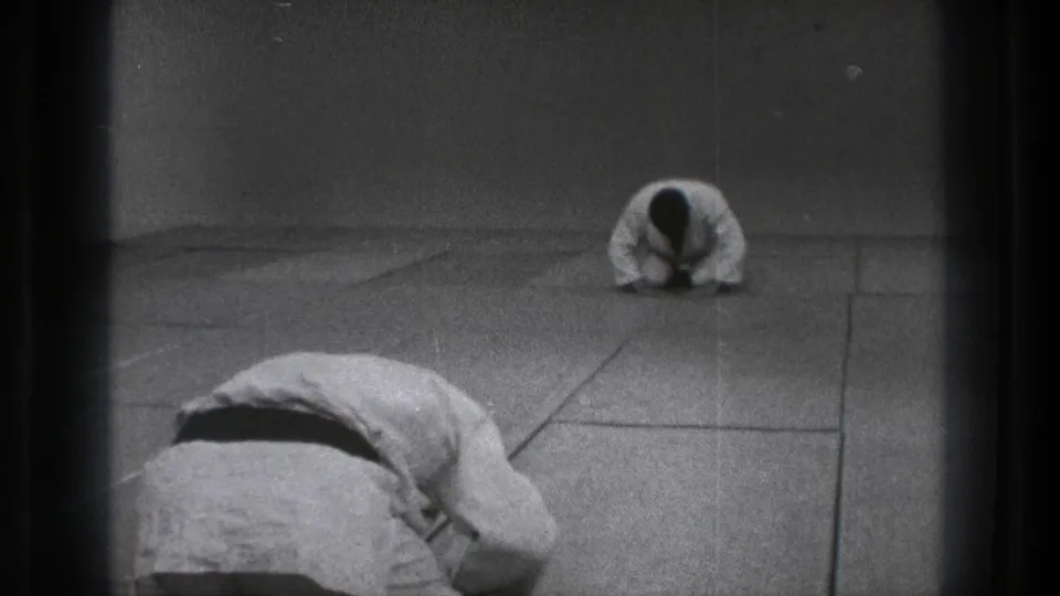 Black-and-white 8mm frame from Tokyo showing a formal martial arts bow across a sparse dojo space.