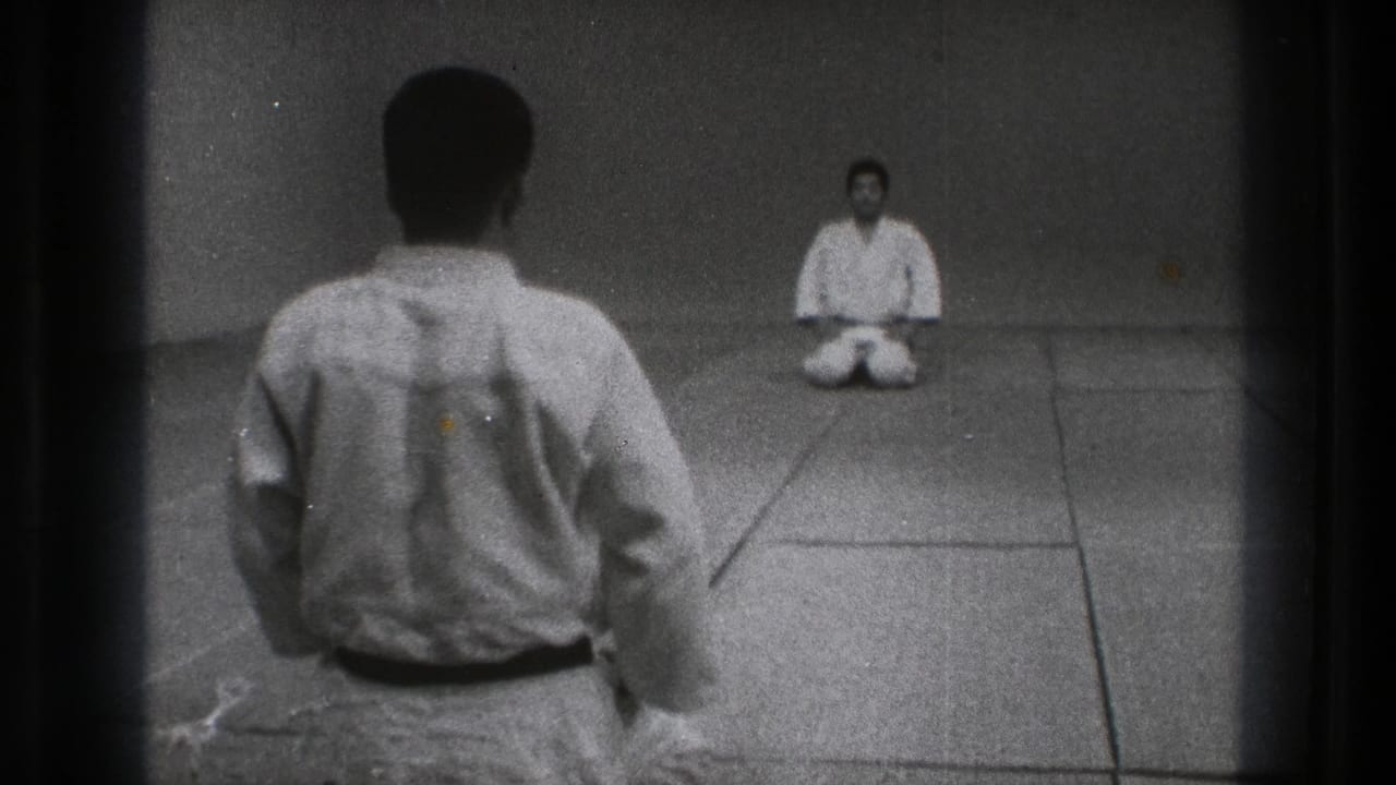 1971 Tokyo 8mm frame showing two men in karate uniforms kneeling across a plain dojo mat.